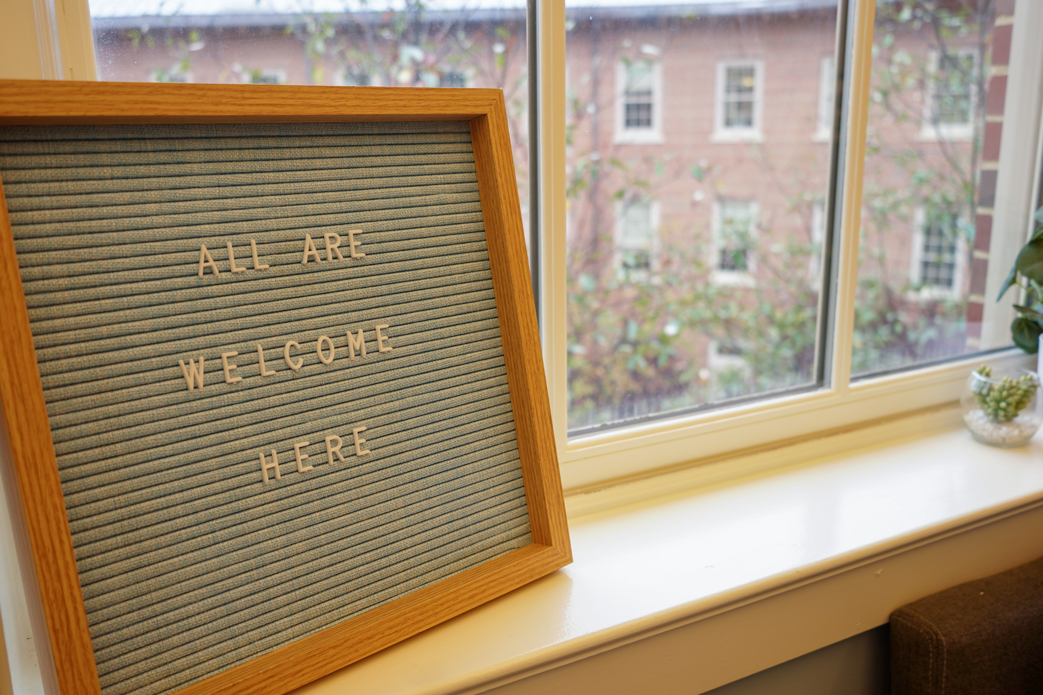 Sign that says, "All are welcome here." on a windowsill.